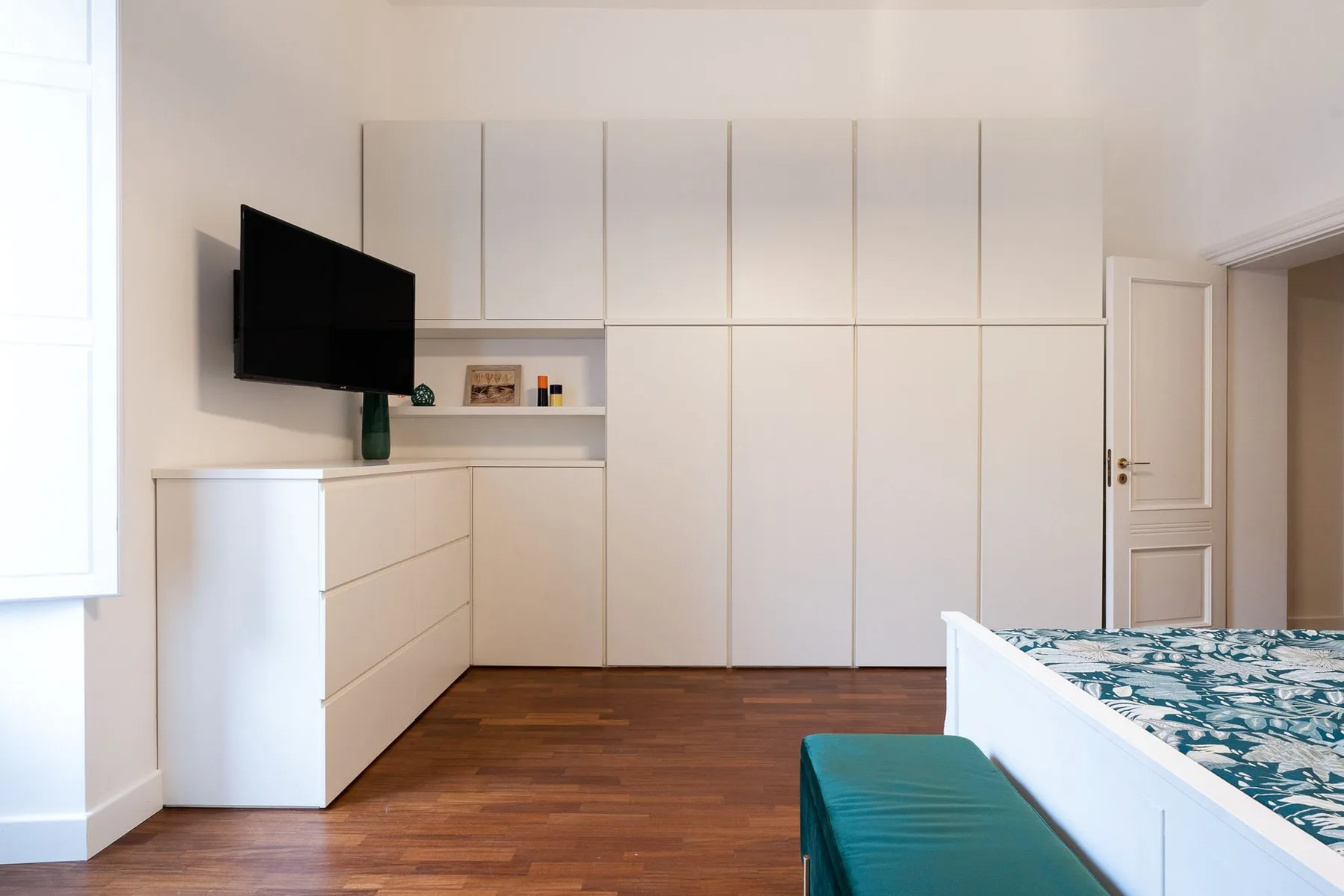 Un dormitorio luminoso con armarios blancos empotrados y una cama.