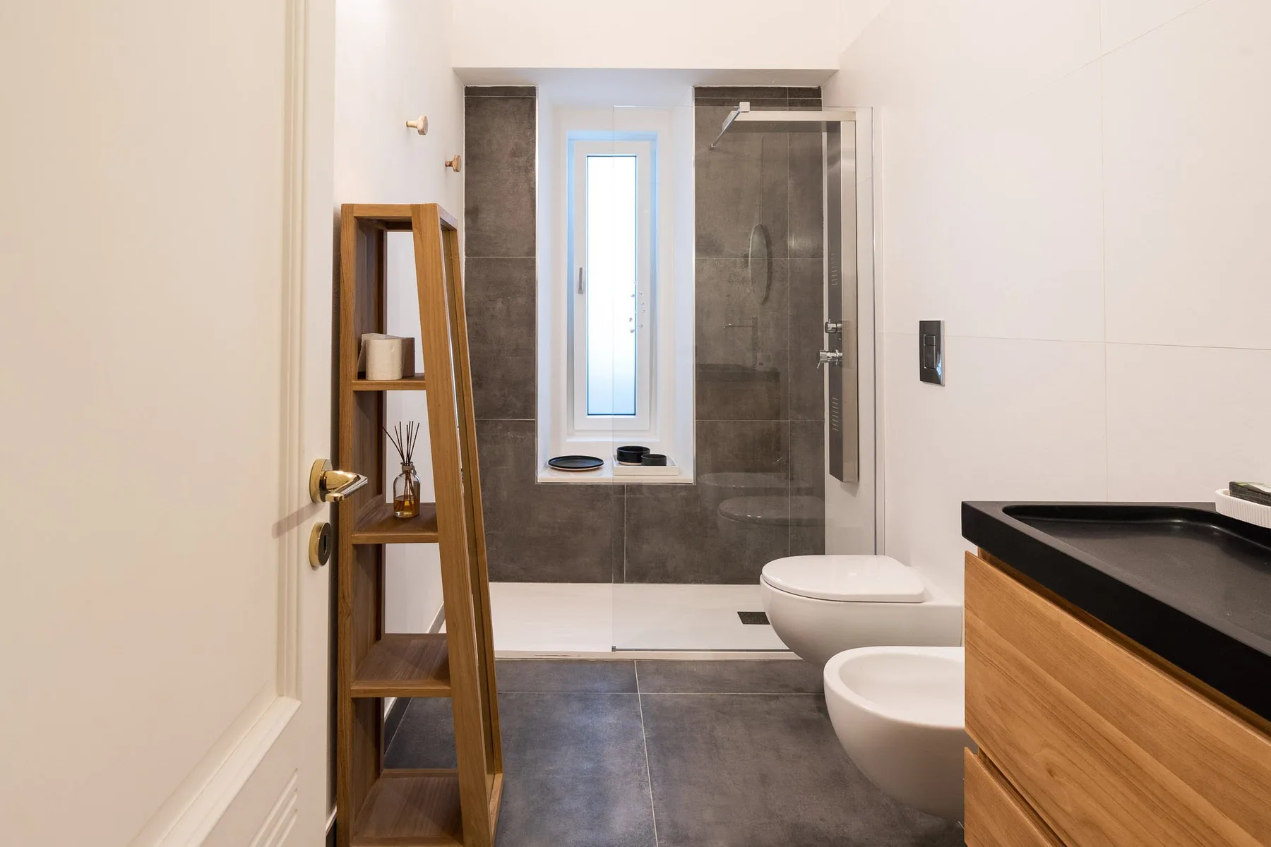 Un baño moderno con ducha de vidrio, inodoro y mueble con frente de madera.