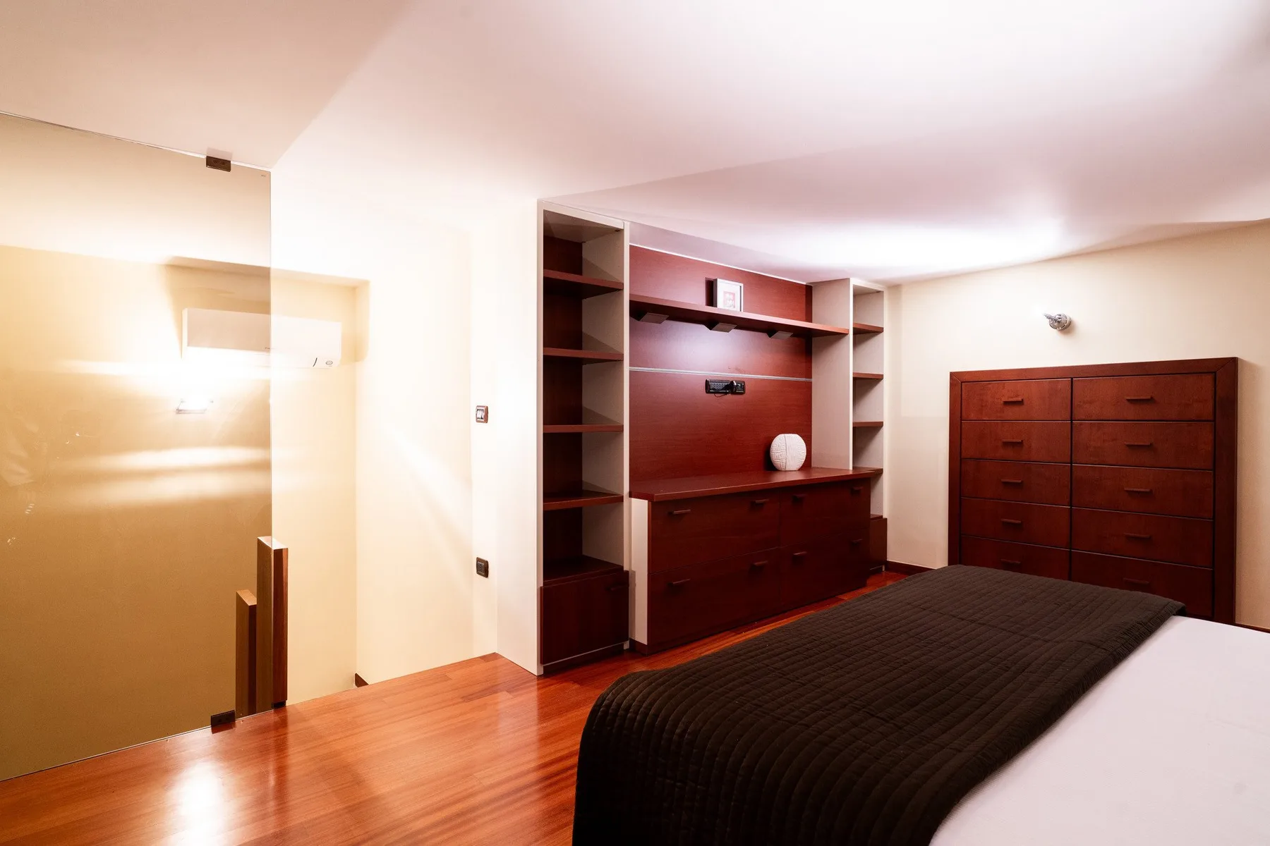Un dormitorio con una cama oscura y estanterías de madera empotradas.