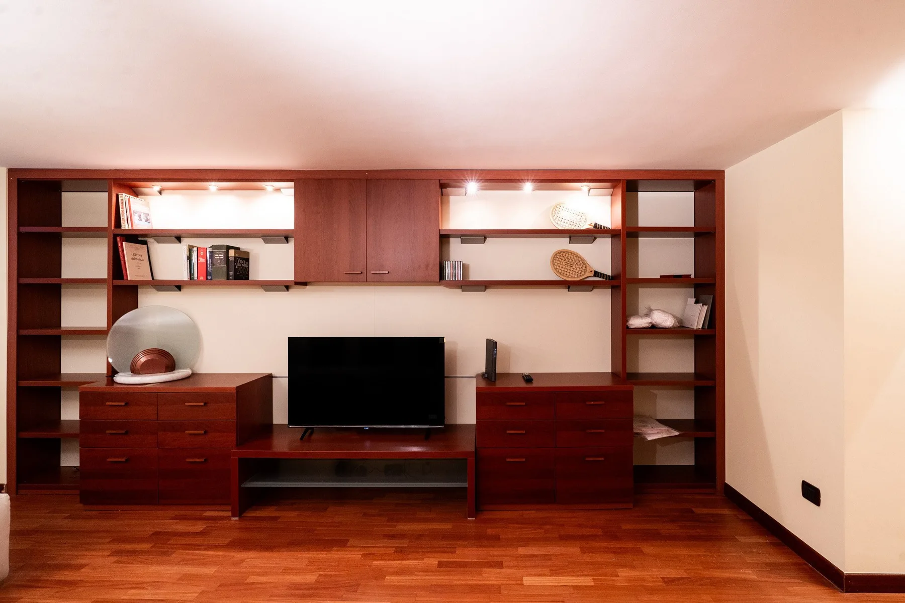 Una pared de sala de estar tiene estantes empotrados, cajones y un televisor.