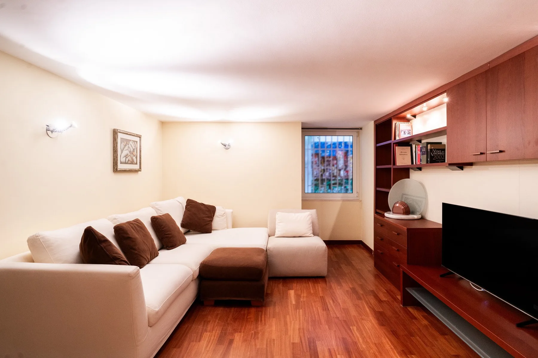 Sala de estar con asientos claros, un televisor y muebles de madera.