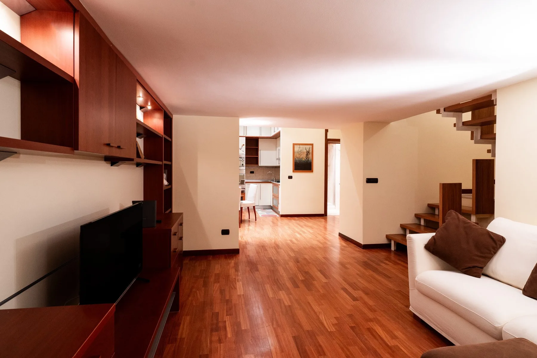 Una sala de estar con suelo de madera, estanterías empotradas y un sofá blanco.