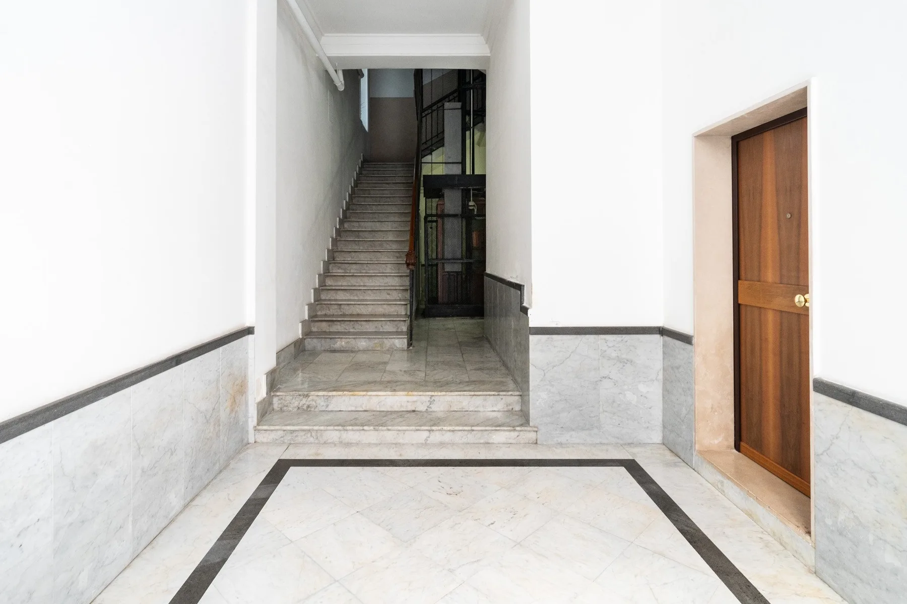 Un pasillo interior de baldosas con una escalera y una puerta de madera.
