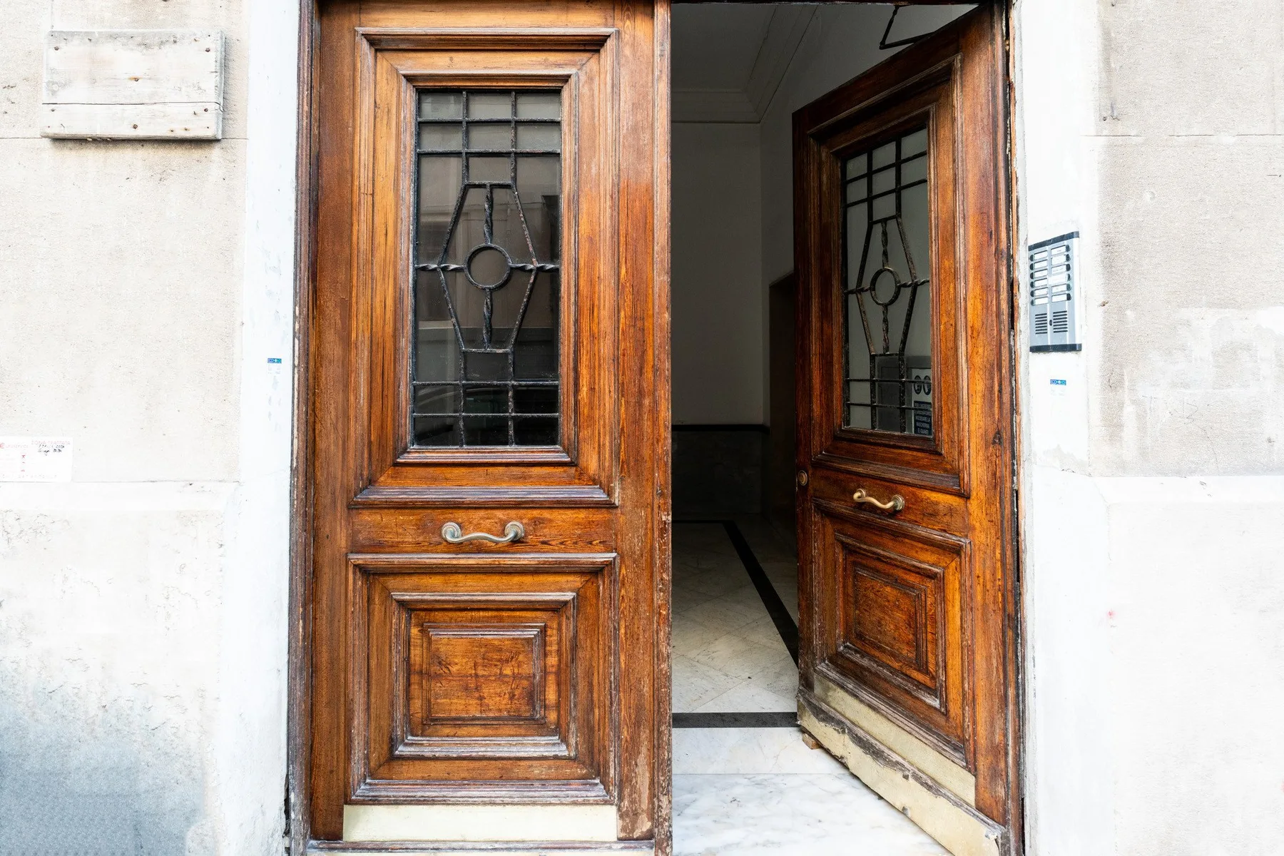 Una puerta de entrada de madera abierta, con paneles de vidrio decorativos, da a un interior oscuro.