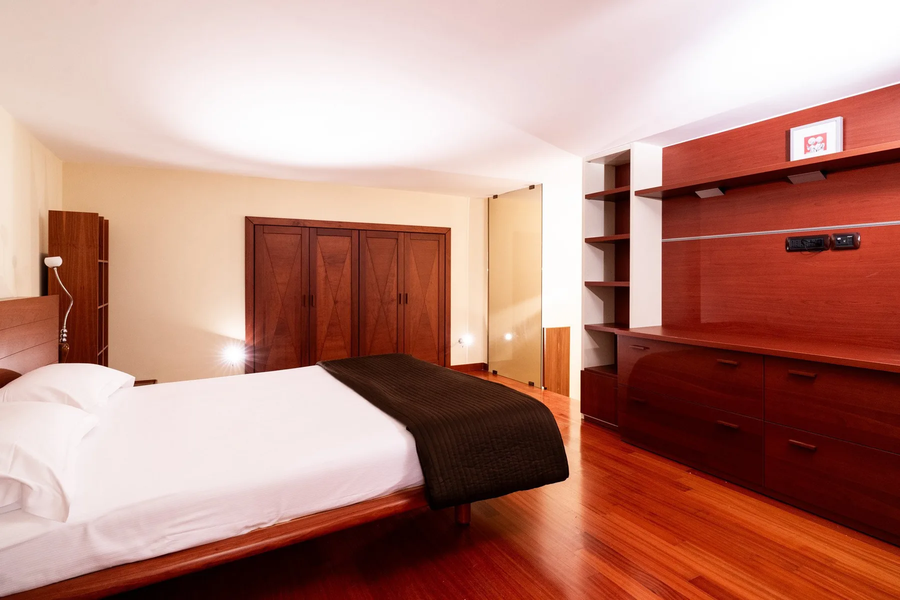 Un dormitorio con una cama grande, ropa de cama oscura y almacenamiento de madera.