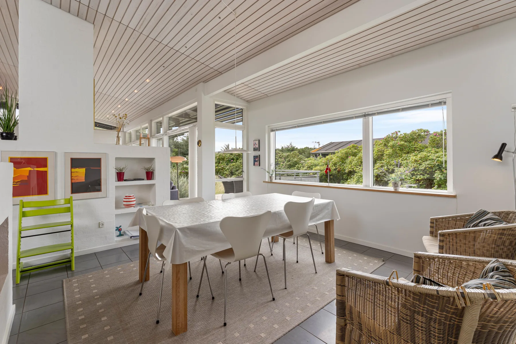 A bright dining and seating area with large windows overlooking greenery.