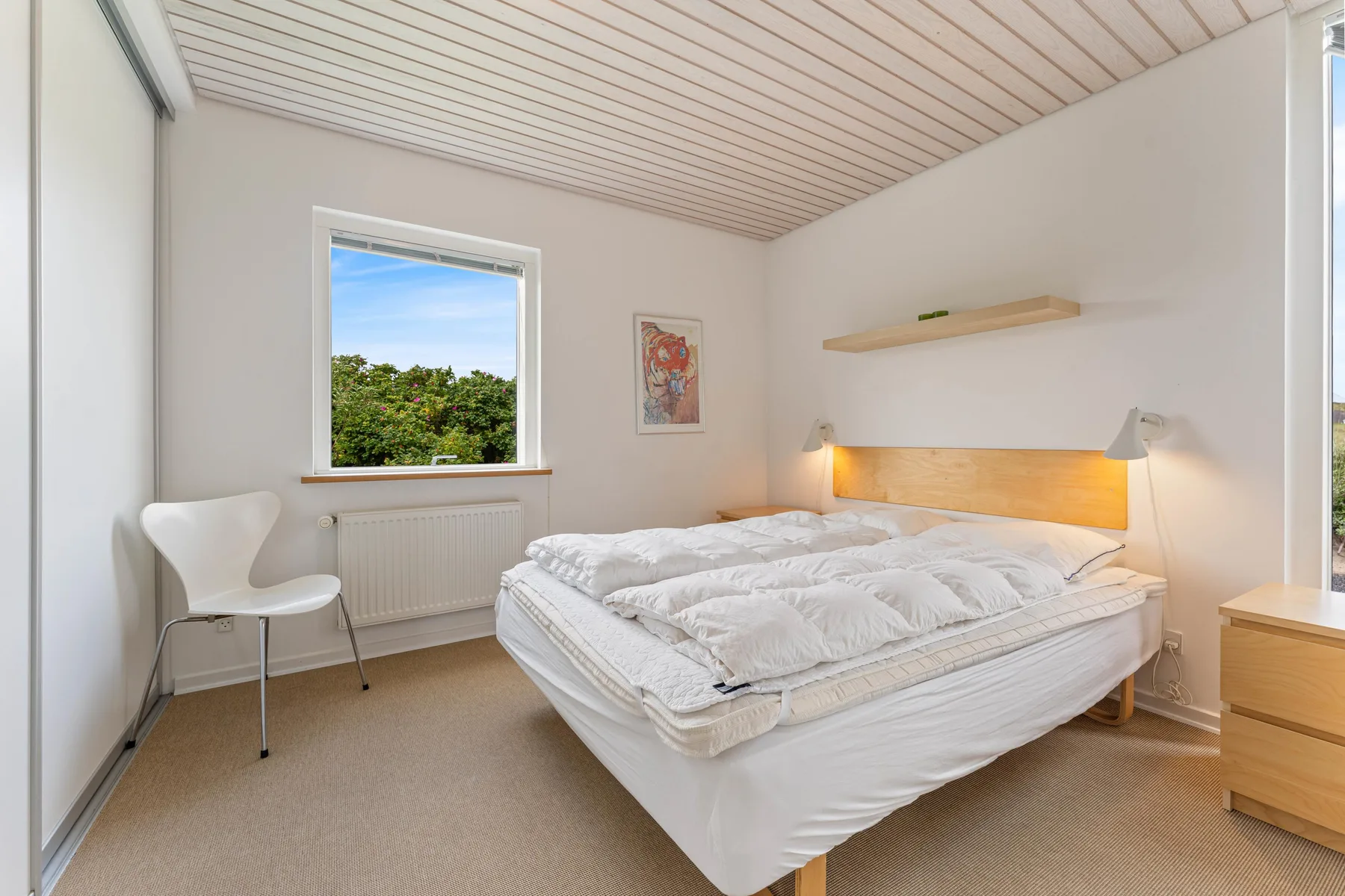 A bedroom with a bed, a window, and a white chair.