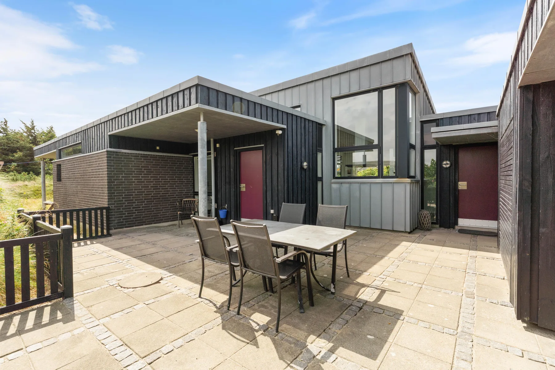 A paved outdoor patio with a dining table and seating beside a modern house.