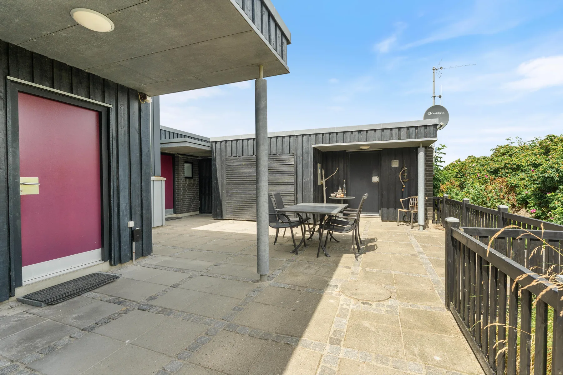 A paved outdoor patio has a dining table and seating beside a modern building.