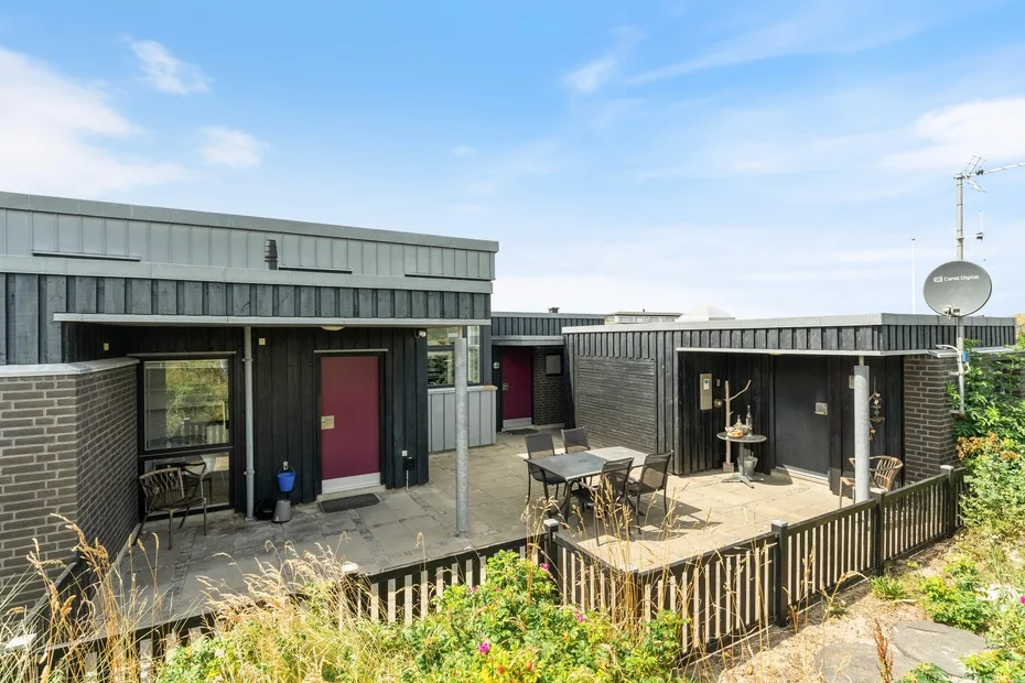 A modern low-rise building opens onto a paved patio with outdoor seating.