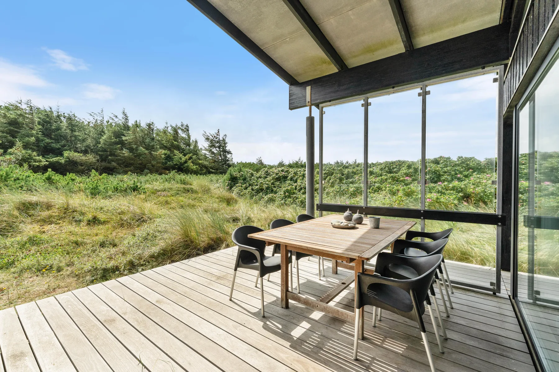 A covered outdoor dining area with a wooden table overlooks green shrubs.