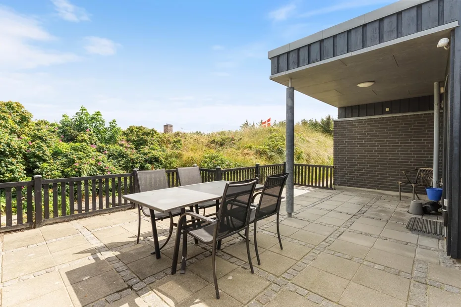 An outdoor patio with a dining table and seating beside a covered area.