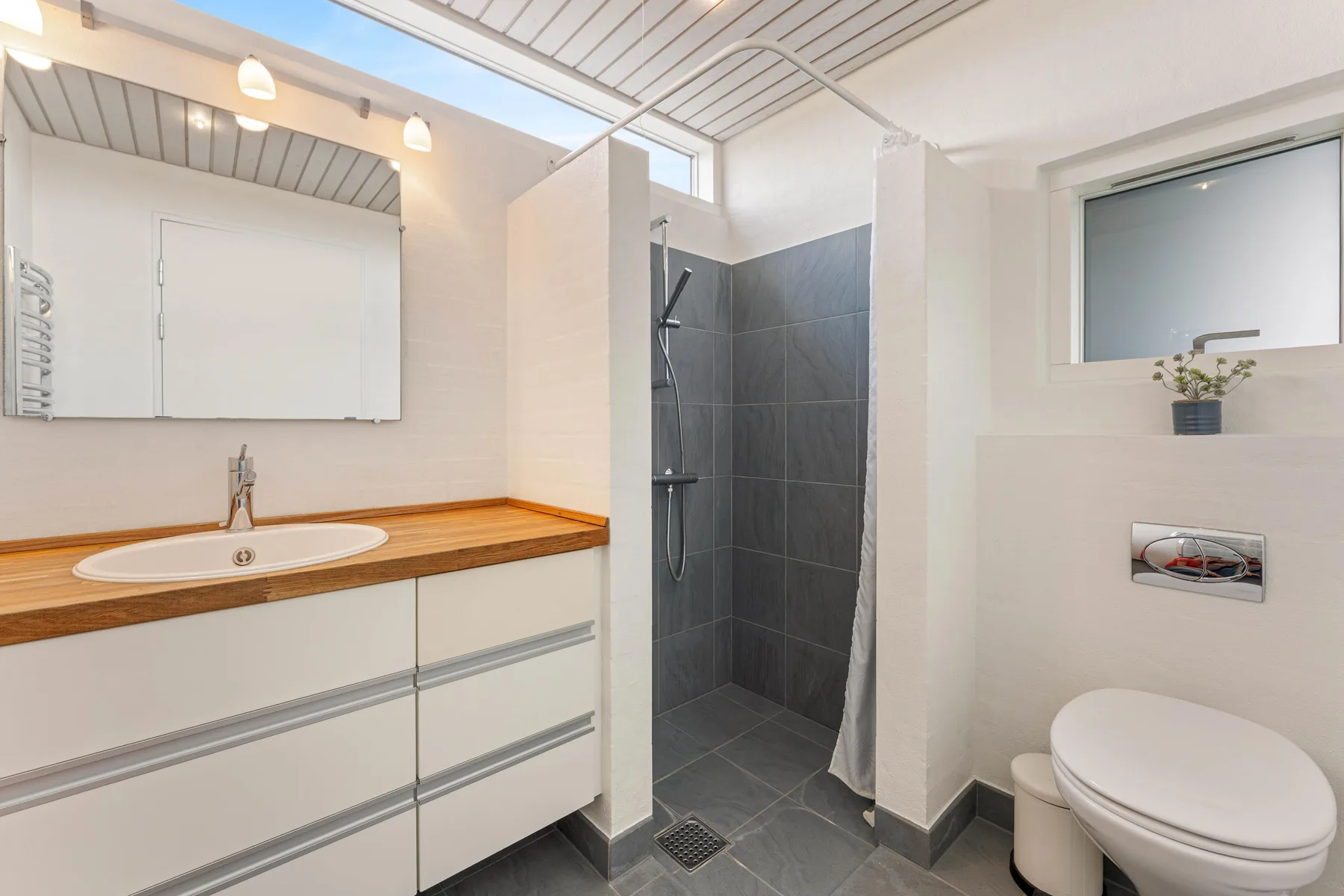 A bathroom with a vanity, mirror, shower, and toilet.