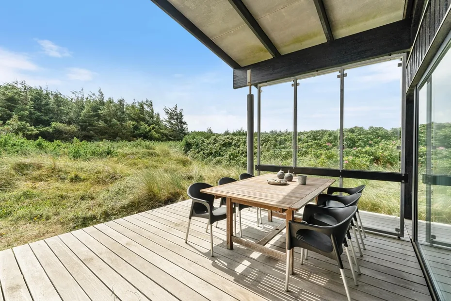 A covered outdoor deck has a wooden dining table and seating overlooking greenery.