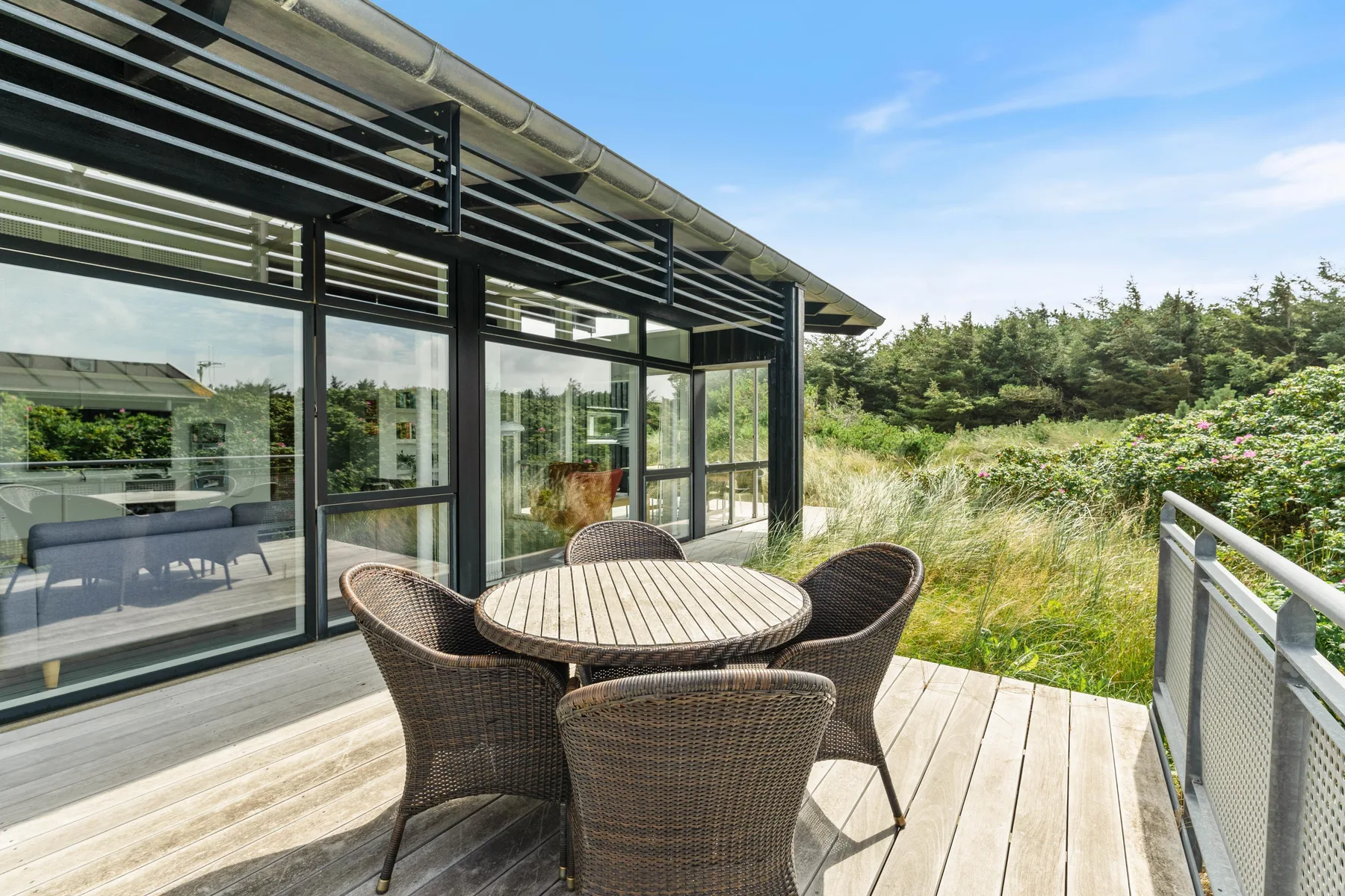 A deck with outdoor seating overlooks grassy vegetation beside a glass-walled building.