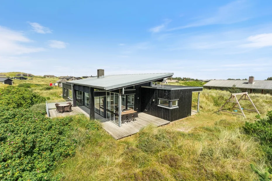 Una casa moderna con grandes ventanas de vidrio se encuentra entre vegetación costera.