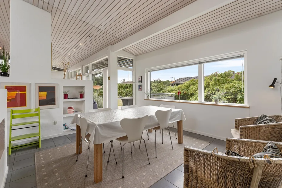 A bright dining area with a table beside large windows overlooking greenery.