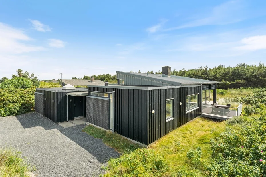 A modern dark-sided house stands beside gravel and green landscaping.