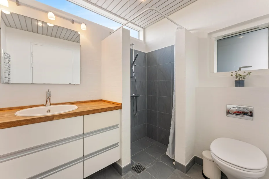 A modern bathroom with a long vanity, sink, shower, and toilet.