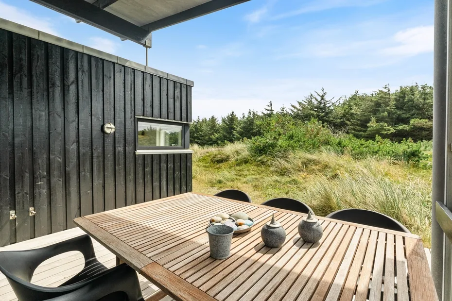 An outdoor dining area with a wooden table beside a dark-sided building.