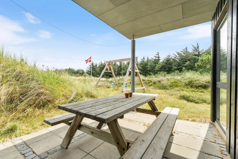 A patio with picnic seating overlooks a grassy garden and a wooden swing.