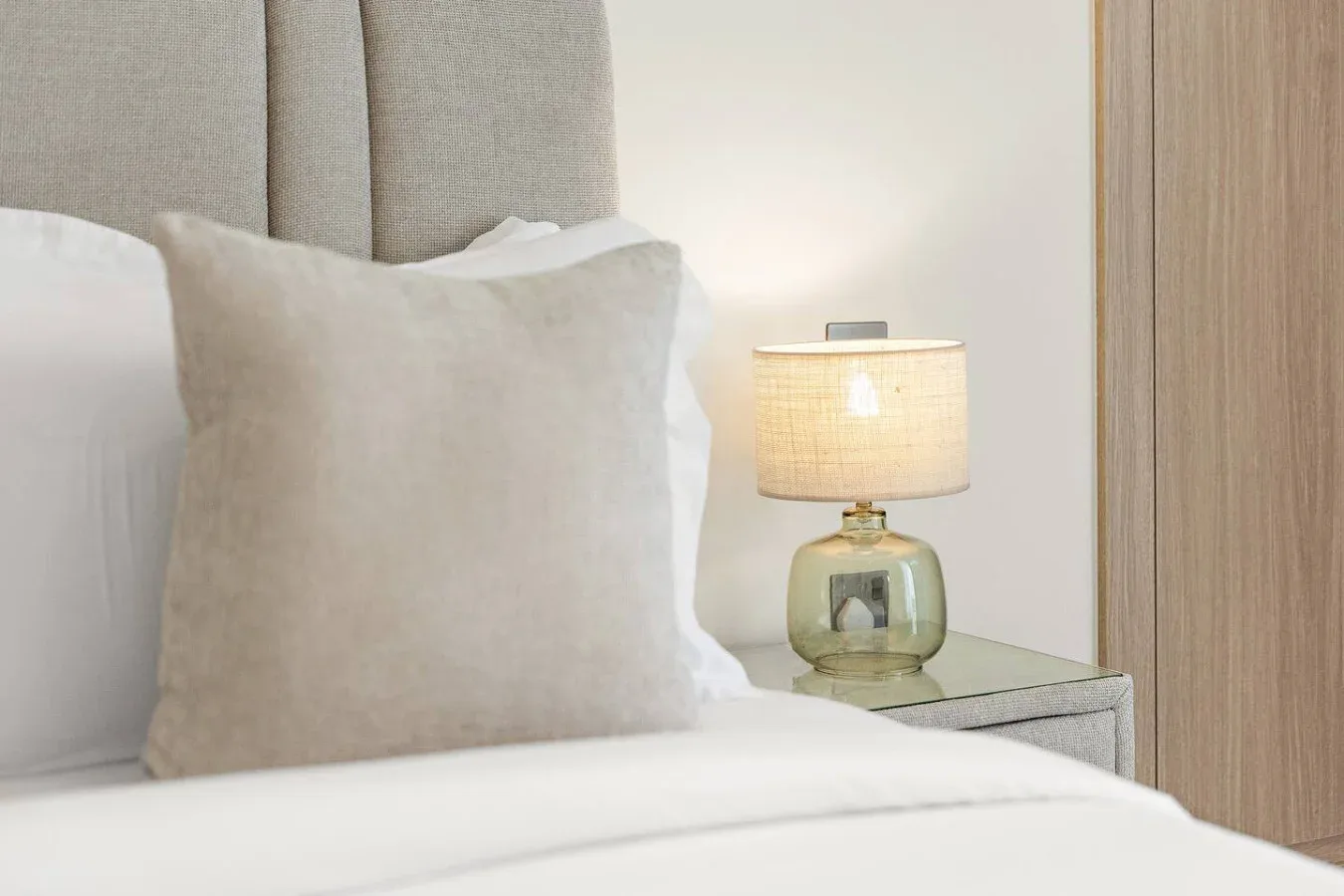 A bedroom with a bed and a lit bedside lamp on a side table.