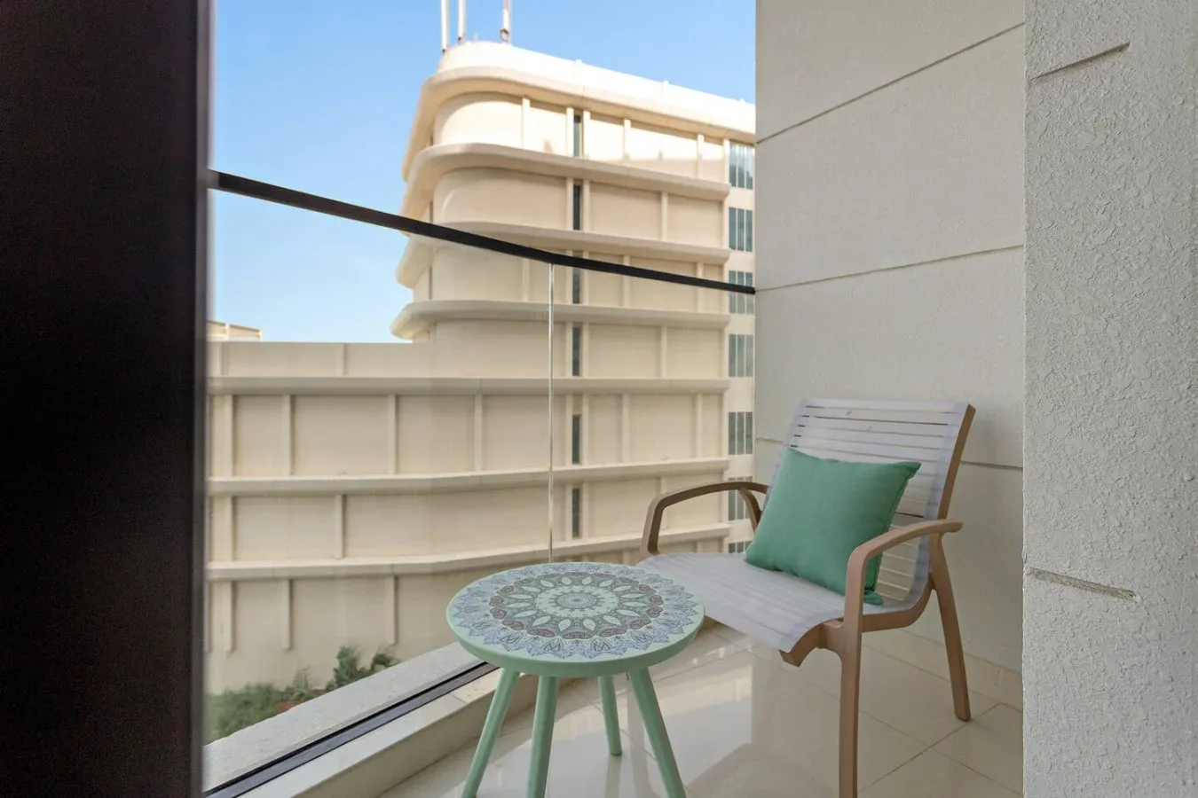 A small balcony with a chair and round table overlooks nearby buildings.