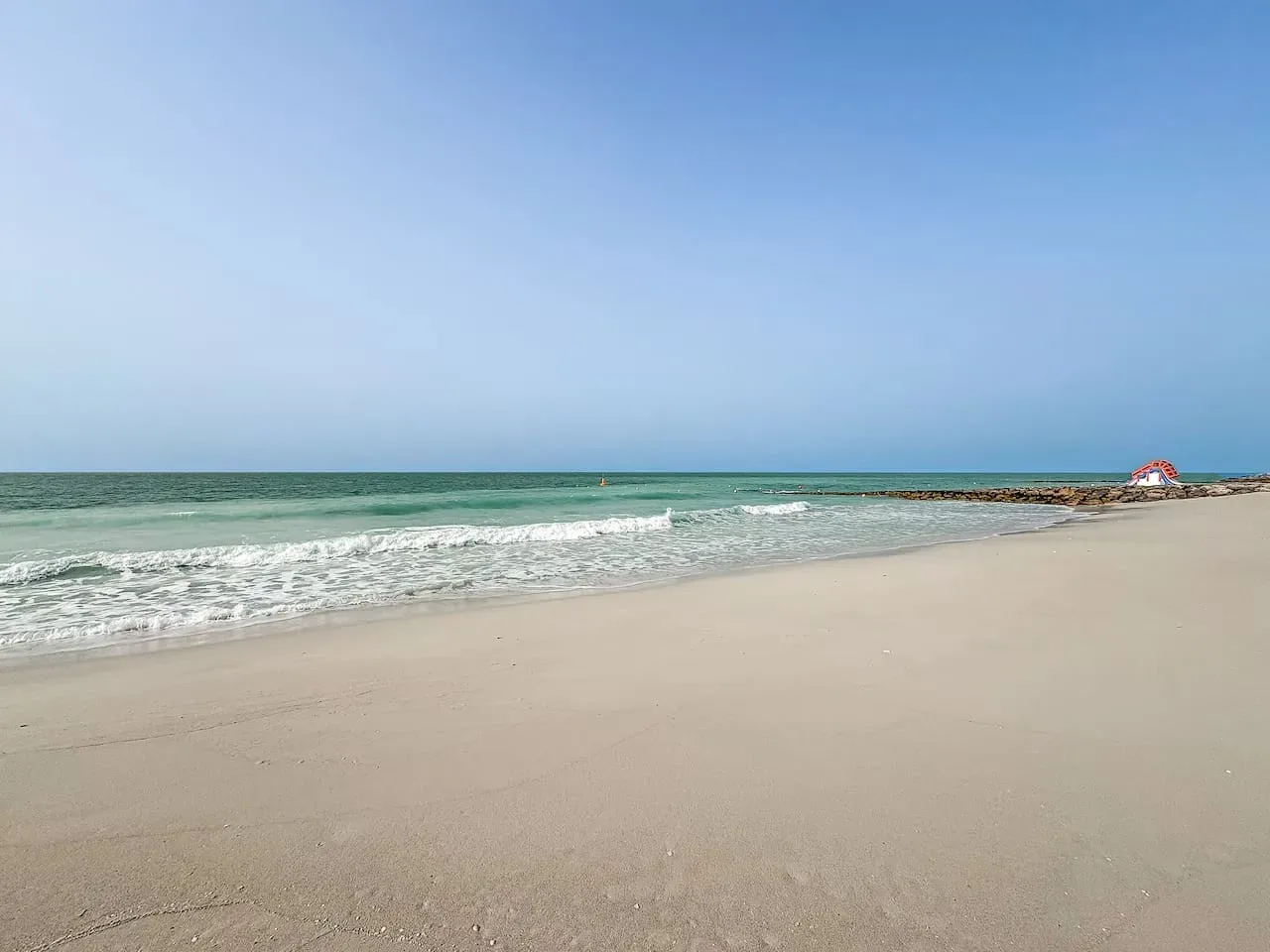 A sandy beach meets calm turquoise water beneath a clear sky.