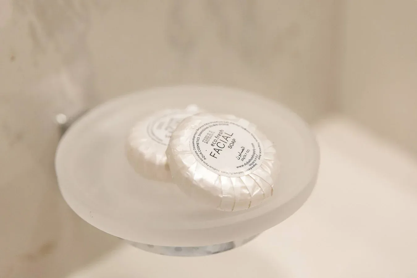 A bathroom soap dish holds two wrapped facial soap bars.