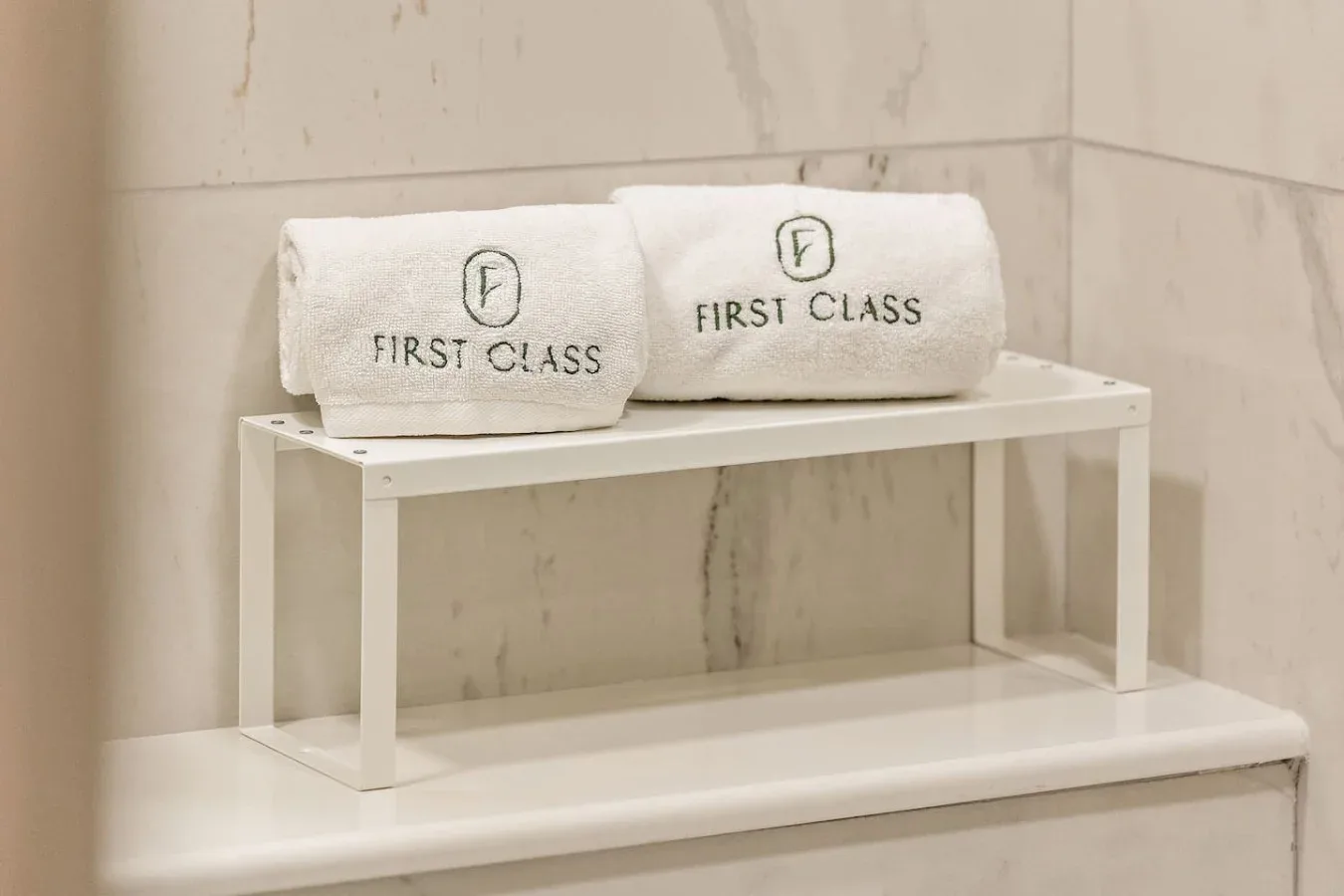 Folded towels sit on a white shelf in a marble-tiled bathroom.