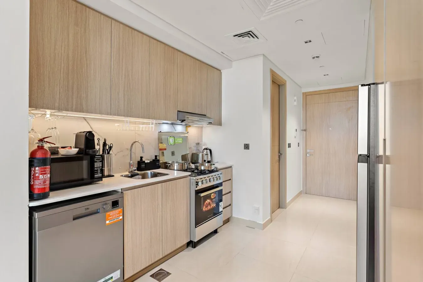 A modern kitchen with light wood cabinets, countertop appliances, and a stainless-steel refrigerator.