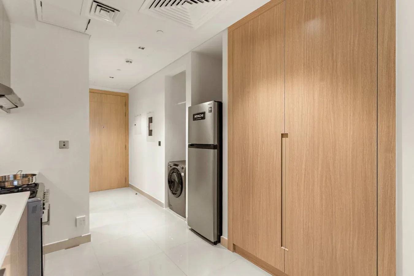 A modern kitchen with light wood cabinetry, a refrigerator, and a washing machine.