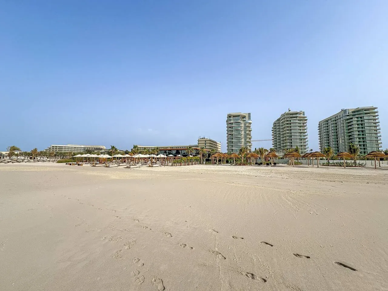 A sandy beach with resort buildings and palm trees in the distance.