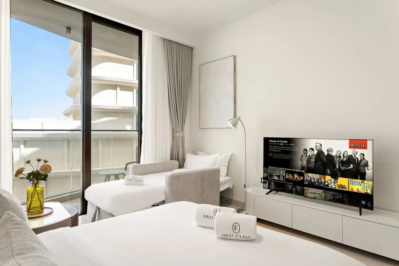 A bright bedroom with beds, a television, and a balcony view.