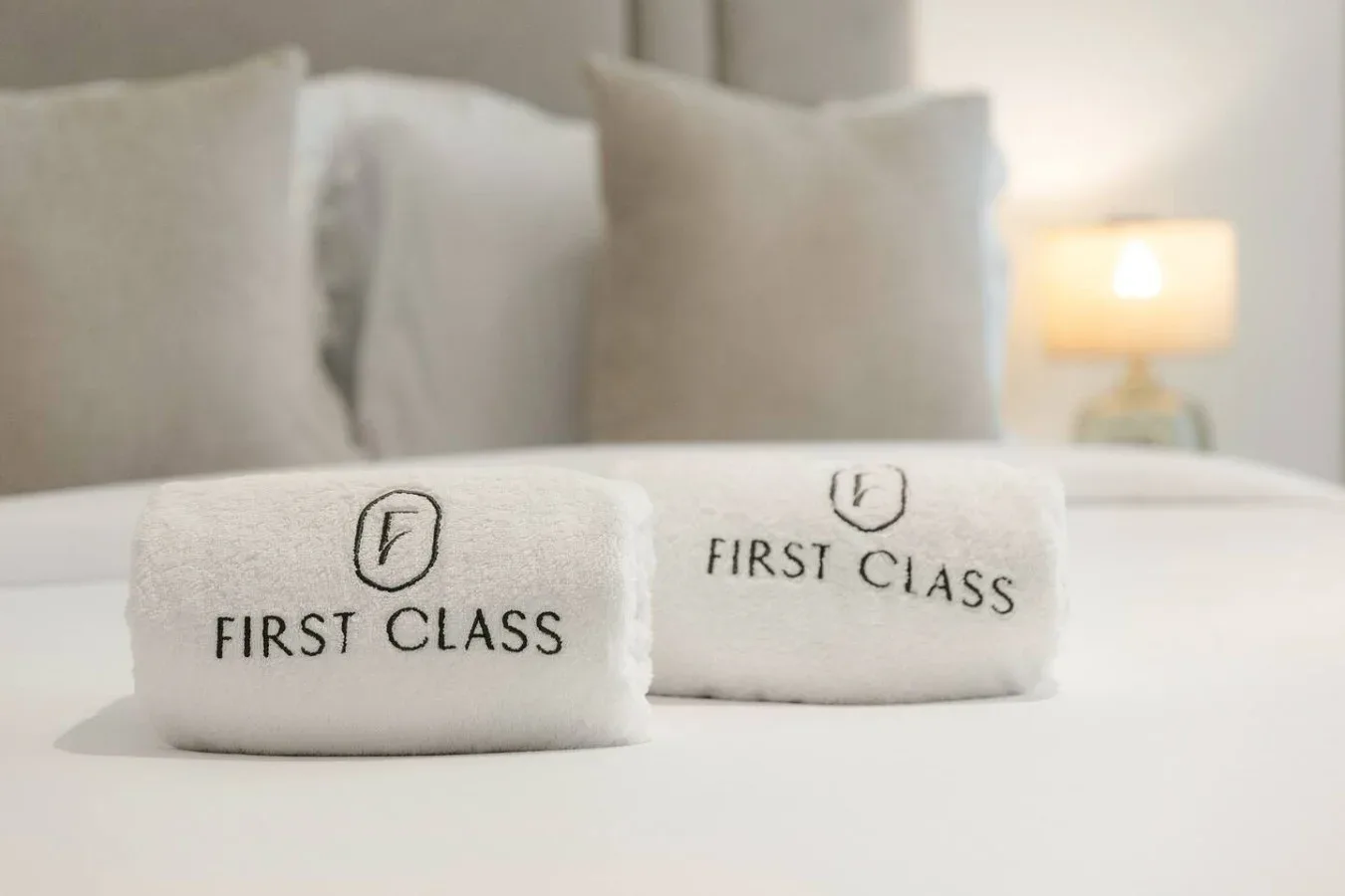 A bedroom scene with folded towels labeled “First Class” on the bed.