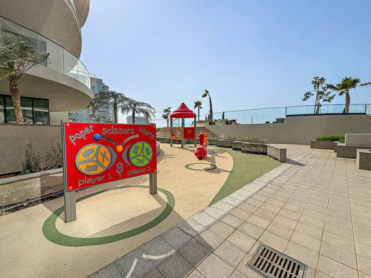 An outdoor play area features a colorful paper-scissors-stone game board and play equipment.