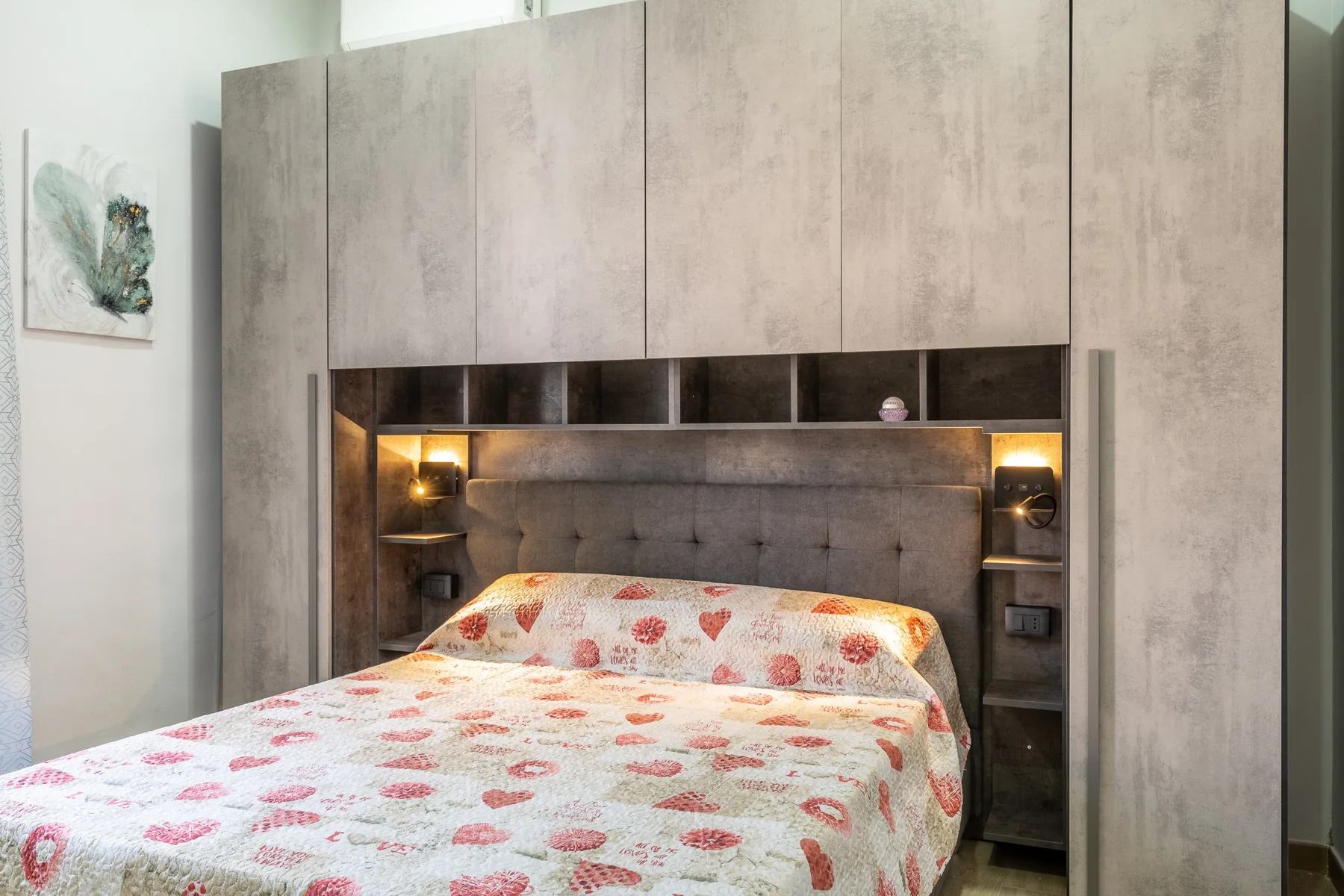 Un dormitorio con una cama doble bajo armarios empotrados y luces cálidas junto a la cama.