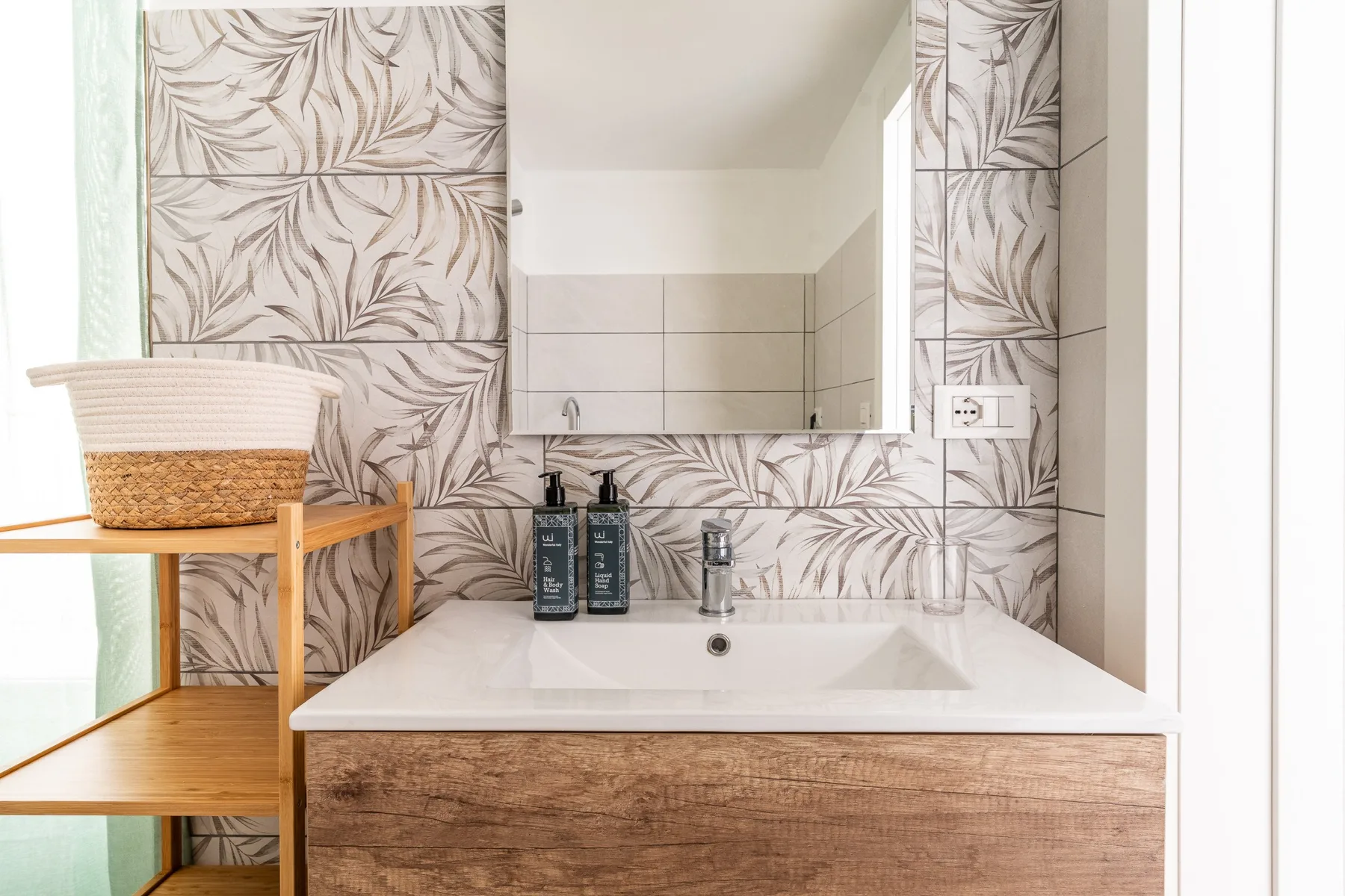 Un tocador de baño con lavabo blanco, espejo grande y azulejos estampados.