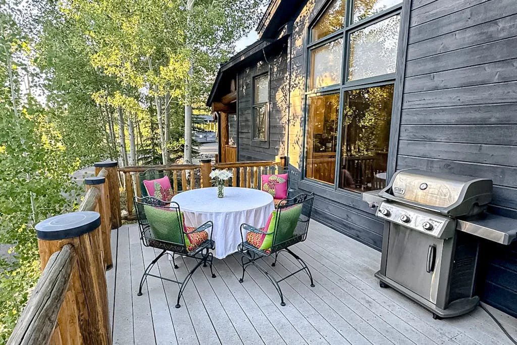 A wood deck beside a dark-sided house has a round dining table and grill.