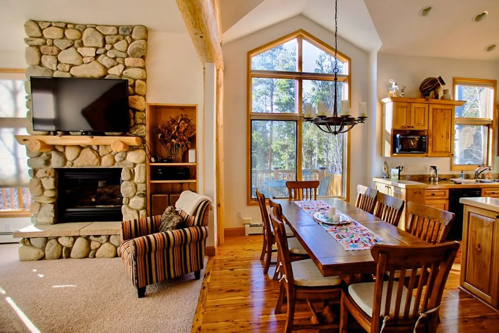 A bright living and dining area with a stone fireplace and wooden table.