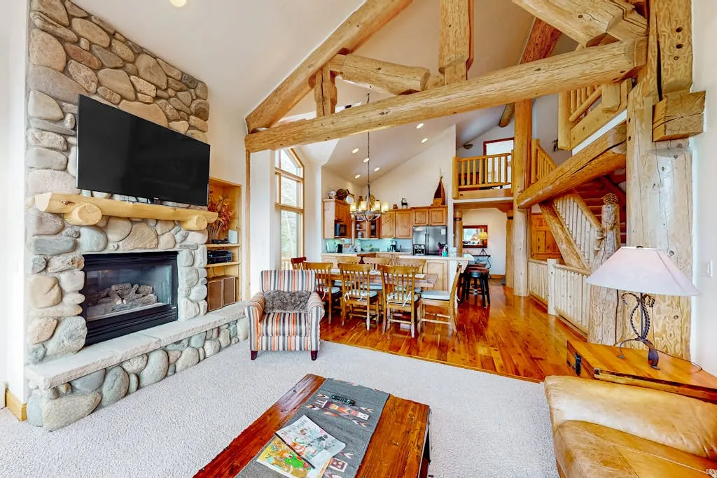 A vaulted living room opens onto a dining area and kitchen, with exposed wooden beams.