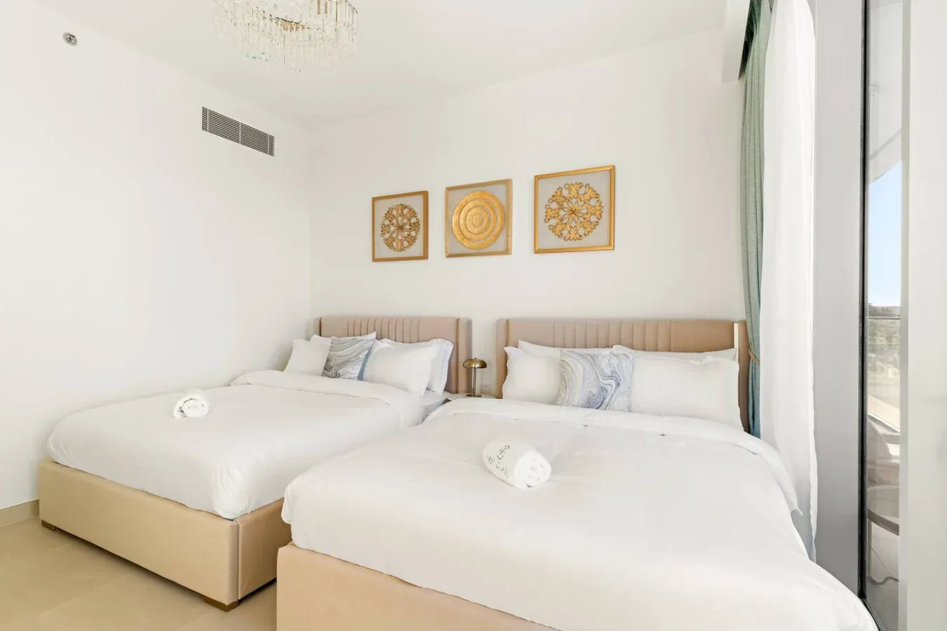 A bright bedroom with two beds and framed artwork above them.