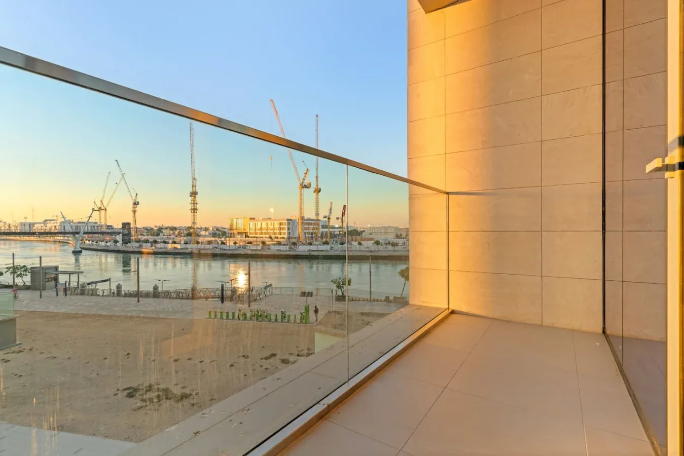 A glass-railed balcony overlooks a waterfront construction site at sunset.