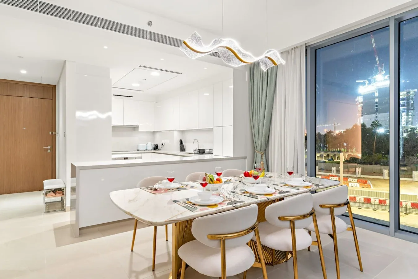A dining area with a set table beside large windows and an open kitchen.