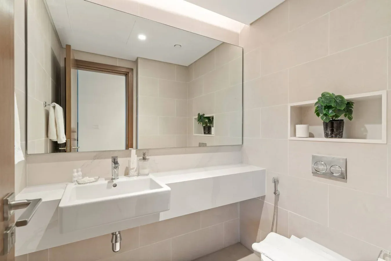 A bright tiled bathroom with a wall-mounted sink and large mirror.