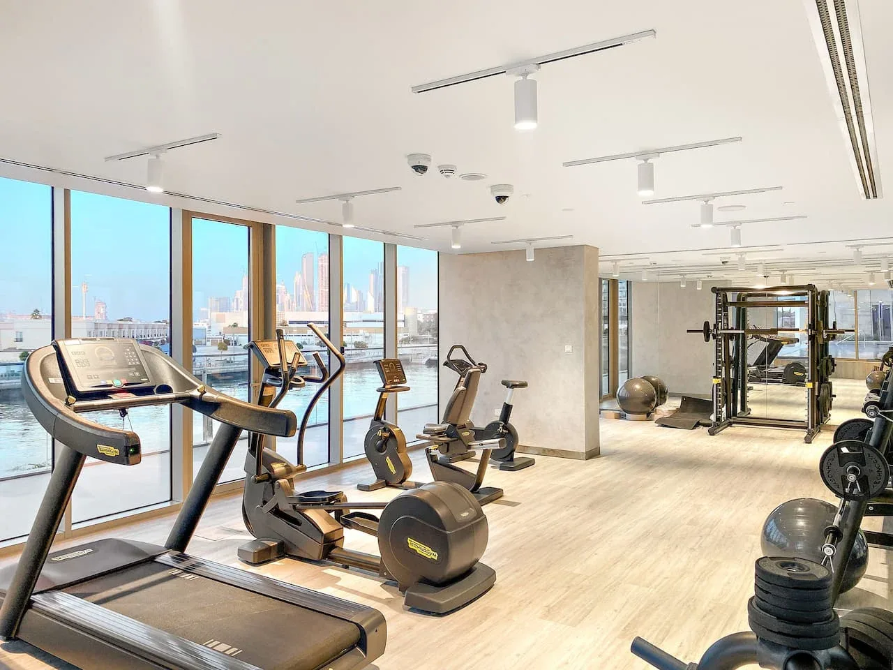 A bright gym with exercise machines beside large windows.