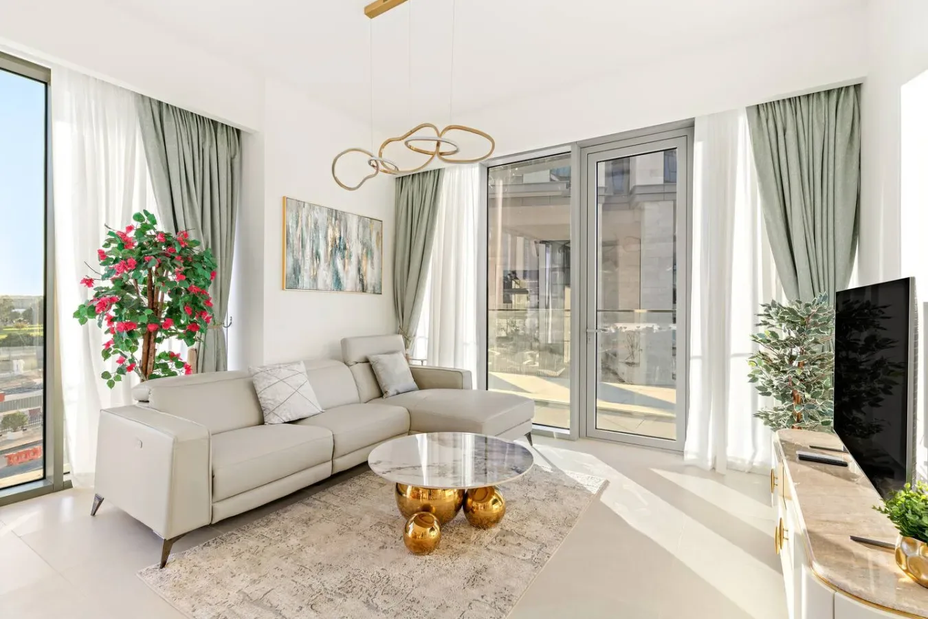 A bright living room with a seating area, large windows, and a television.