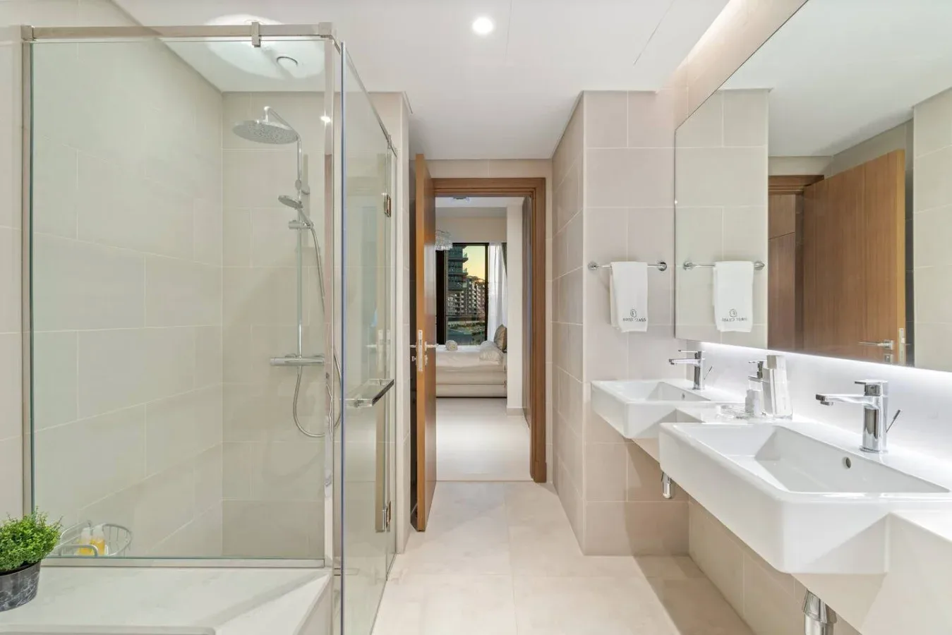 A bright bathroom with a glass shower and twin sinks along the wall.