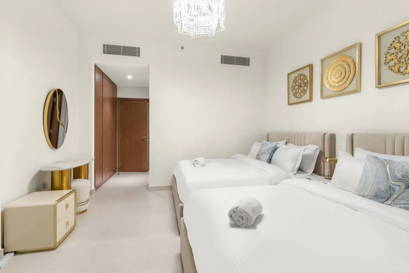 A bright bedroom with two beds, white bedding, and framed wall art.