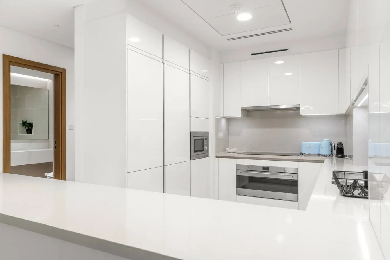 A bright white kitchen with glossy cabinets and a wide foreground counter.